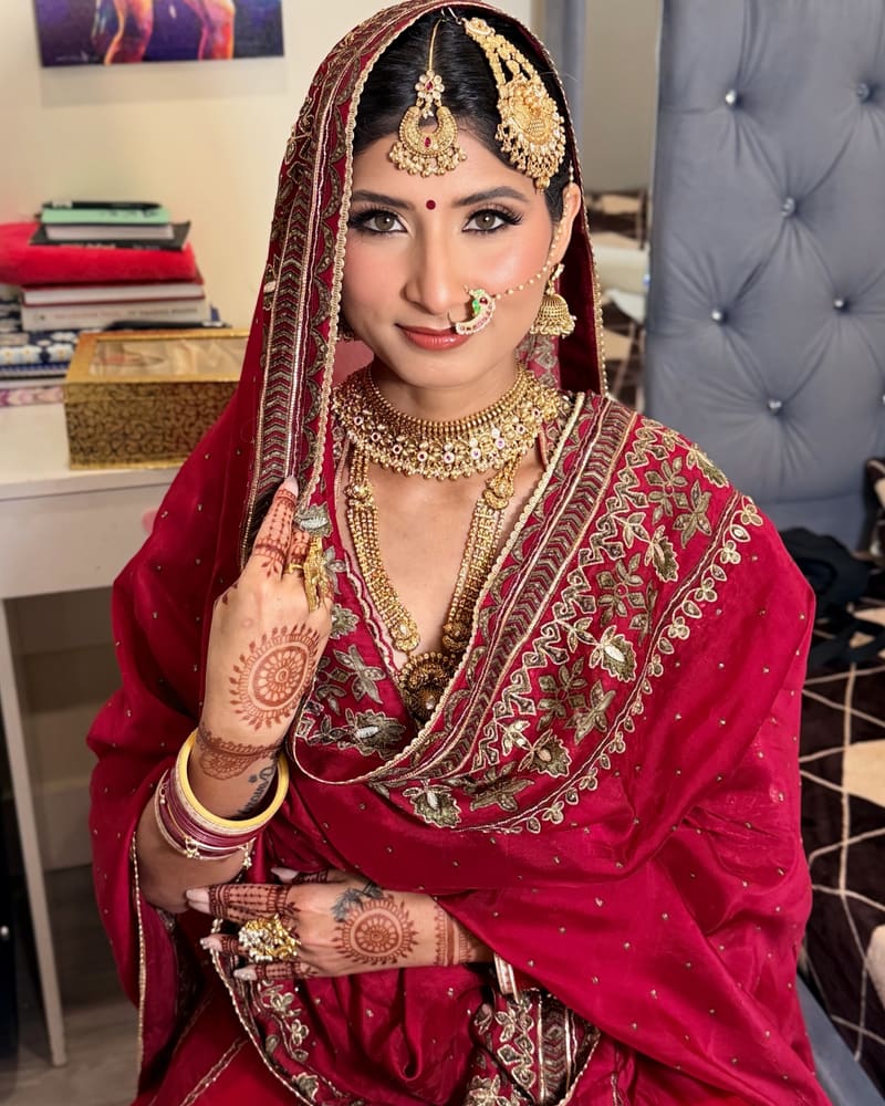 Bride in a deep red embroidered dupatta with a gold necklace and nath