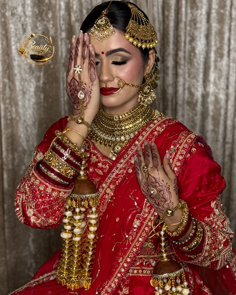 Bride in a red lehenga with gold kaleere and a red dupatta, covering half her face with her hand
