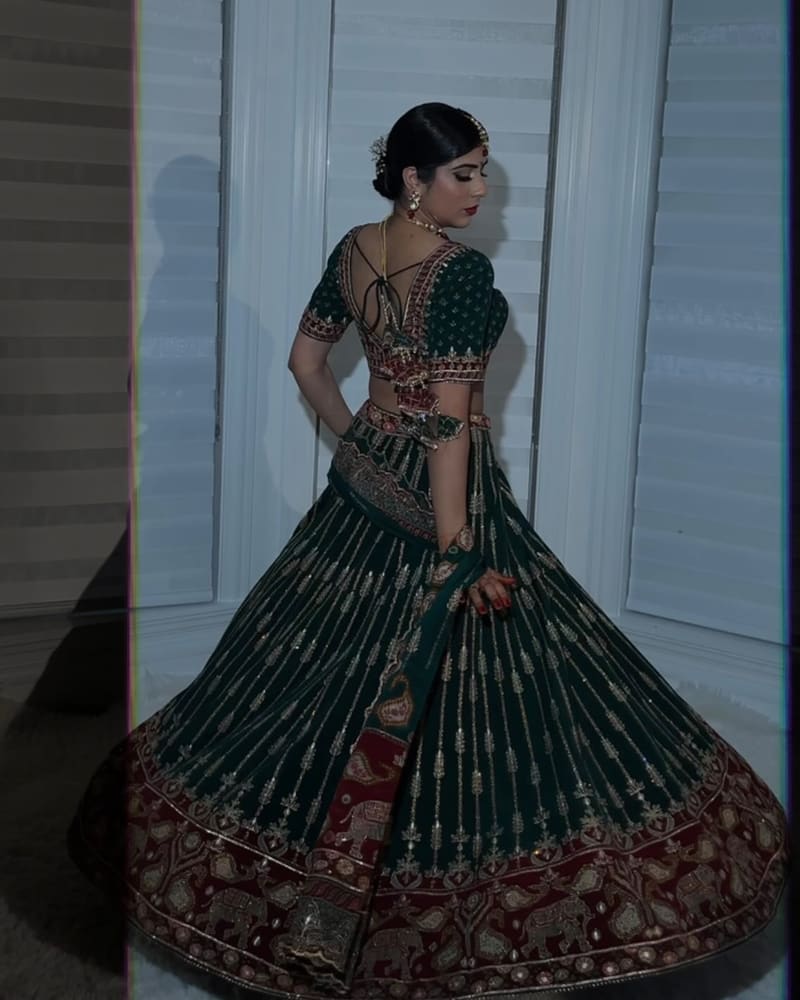 Back view of a woman twirling in a deep green and red lehenga