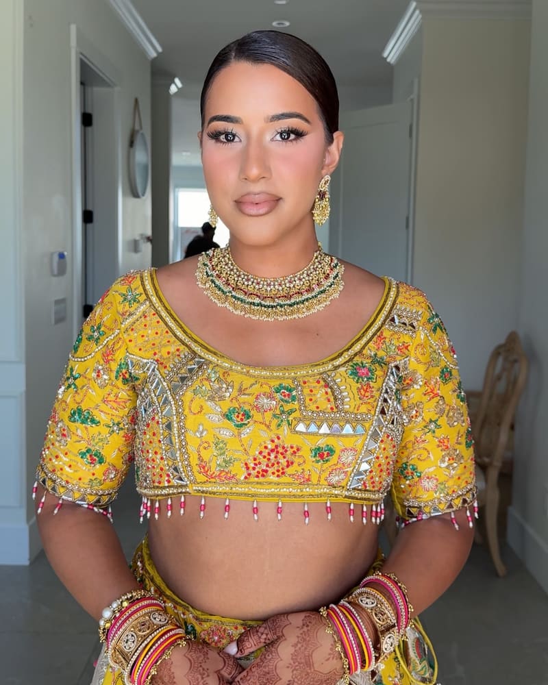 Bride in a yellow mirror work jaggo blouse with a gold necklace and henna