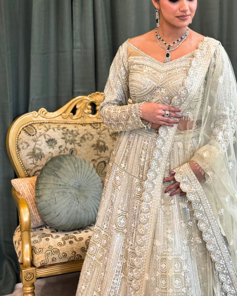 Woman in an ivory sequinned lehenga standing beside a gold carved chair