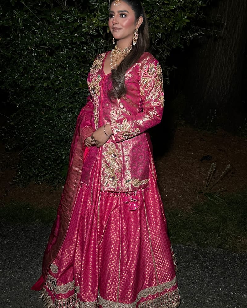 Bride in a fuchsia brocade lehenga with a long jacket top, photographed outdoors at night