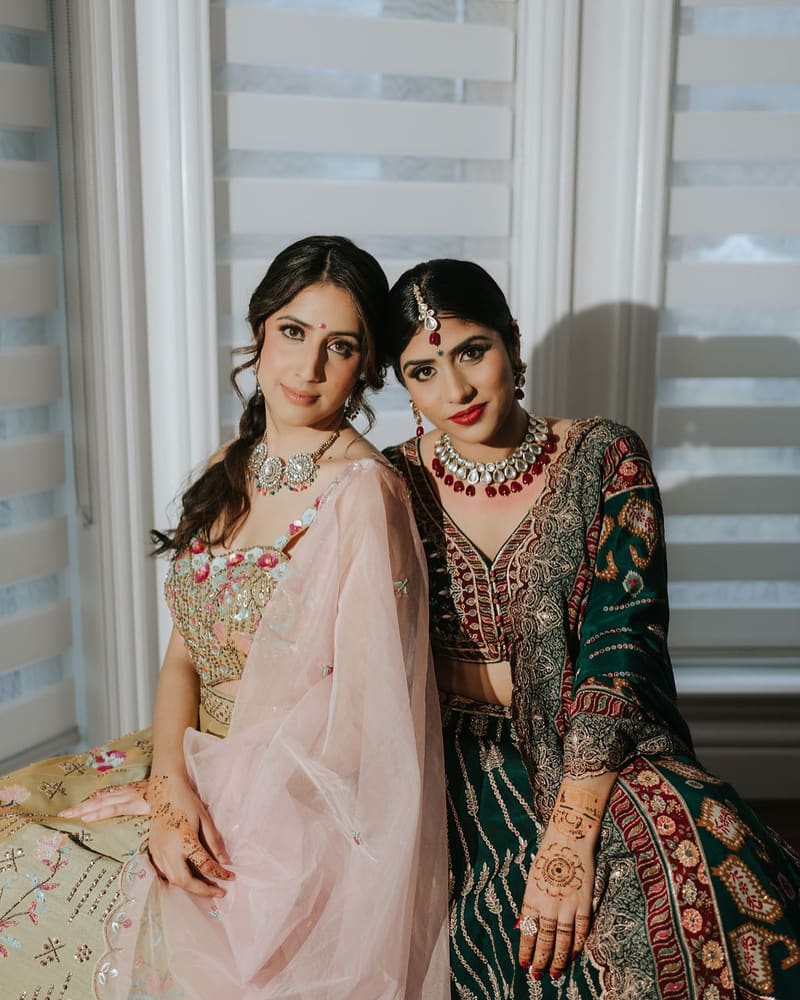 Two sisters posing together, one in blush and gold, one in deep green and red